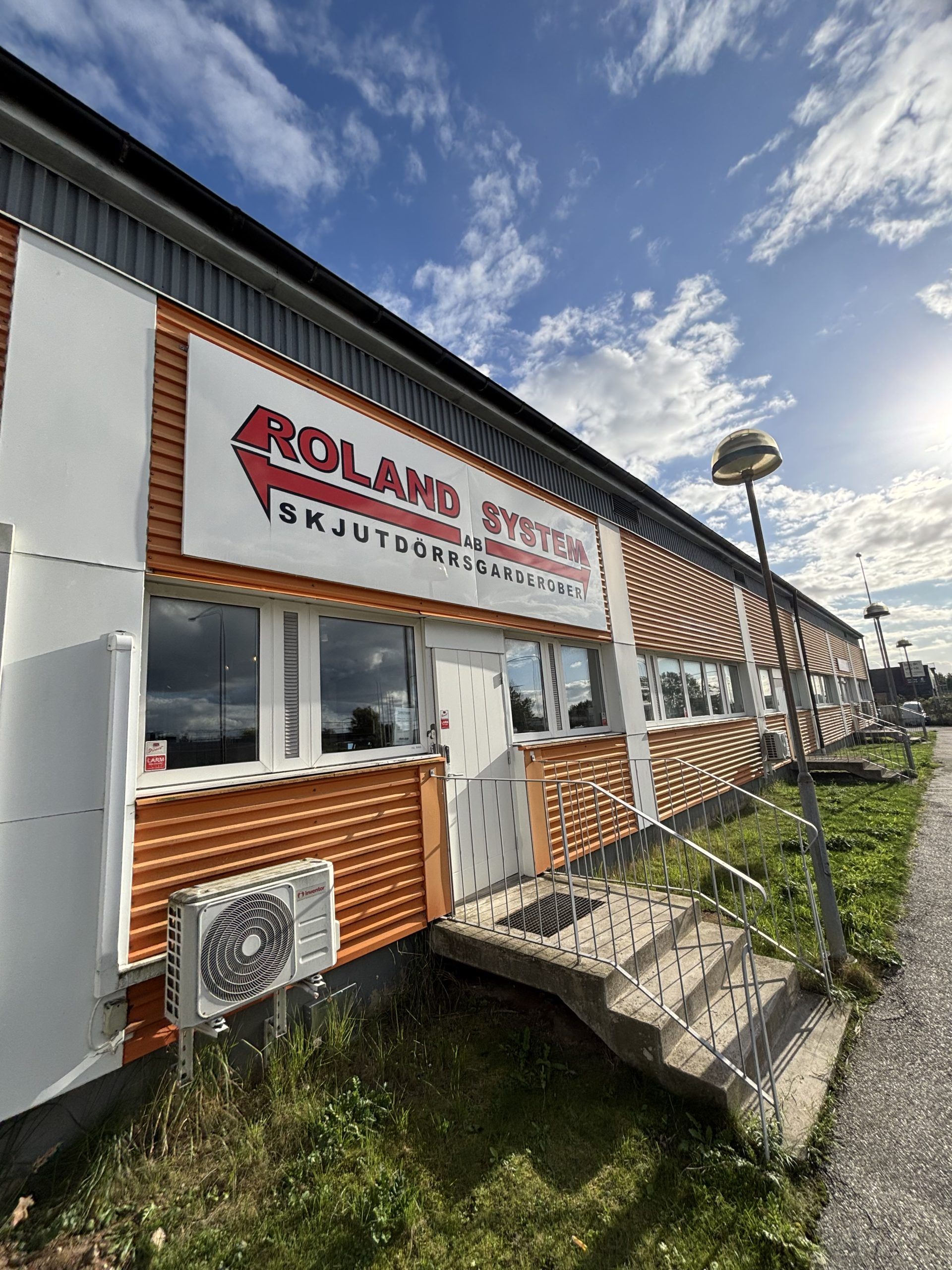 Single-storey building with orange cladding and a large Roland System sign above the windows and entrance.