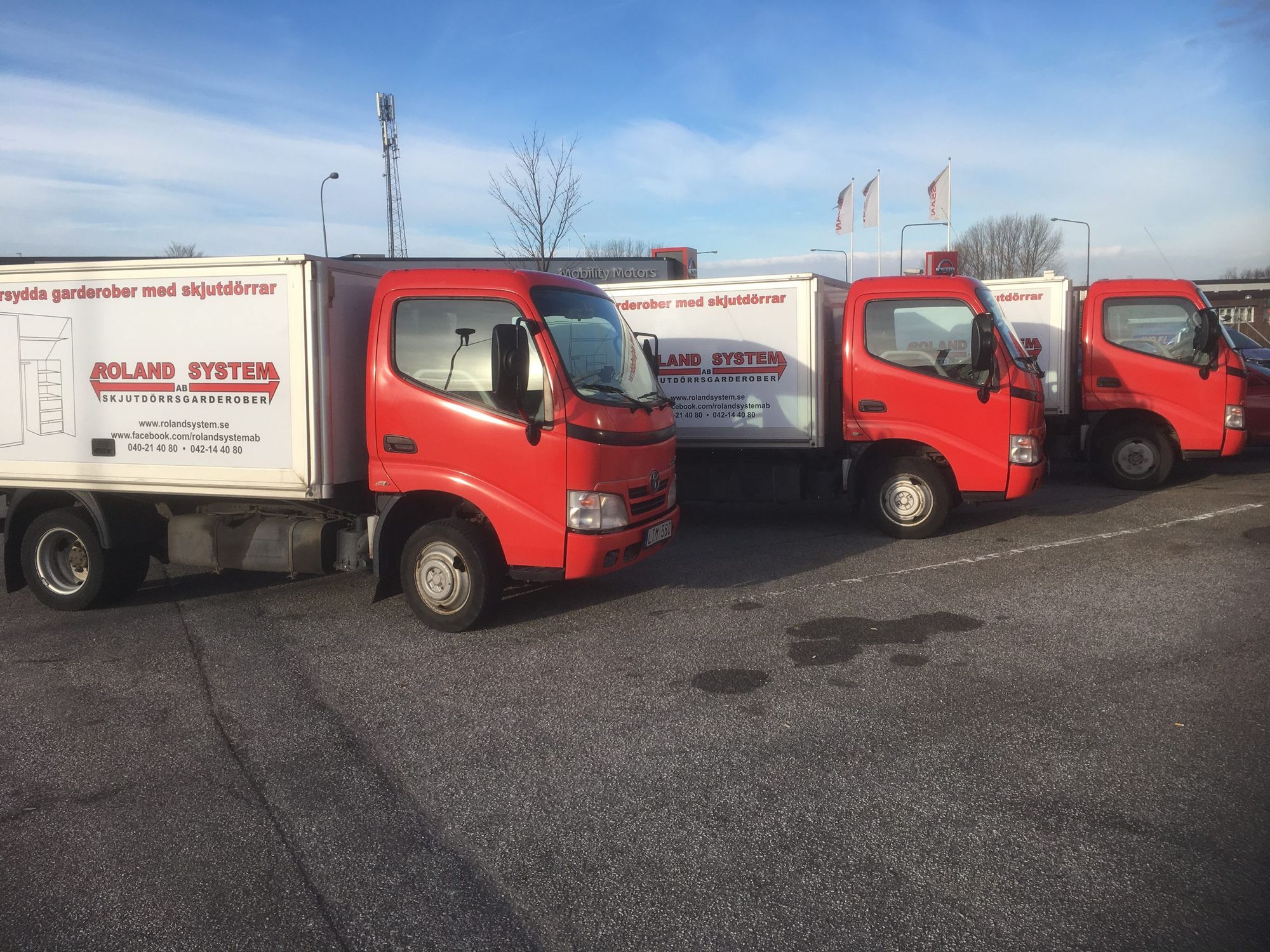 Three red Roland System delivery trucks with white boxes, parked on a paved lot.