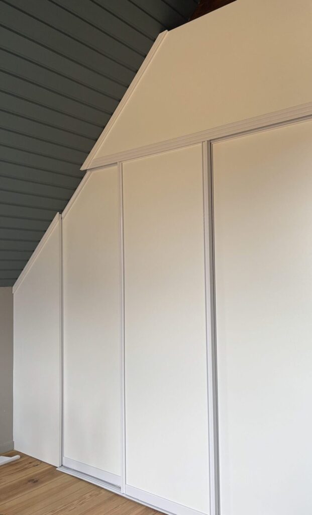 White sliding doors fitted under a sloped ceiling, with the top of the doors cut at the slope.