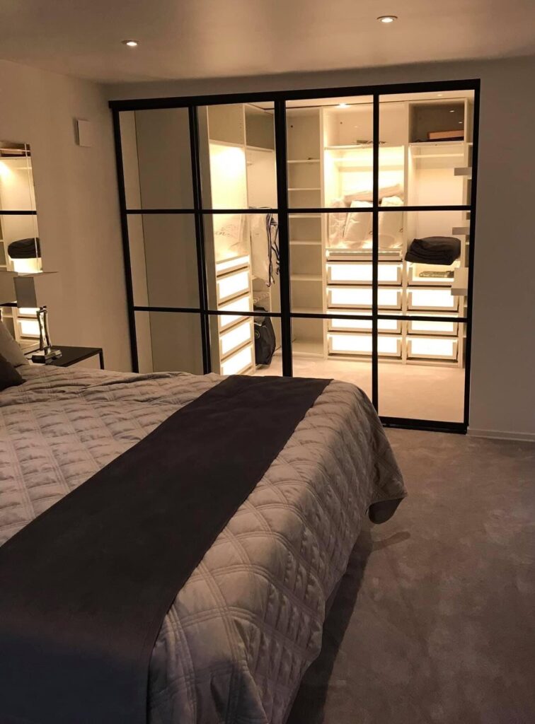 Bedroom with a black-framed glass wall and a lit wardrobe behind
